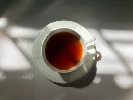 Symbolfoto Teetasse Tasse mit Tee auf einem Tisch, umgeben von sanften Lichtreflexen.