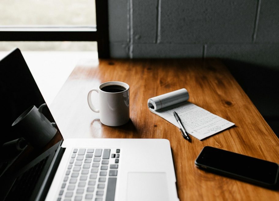 Symbolfoto Schreibtisch mit Laptop, Smartphone, Kaffeebecher Schreibtisch mit Laptop, Kaffeetasse, Notizblock und Smartphone.