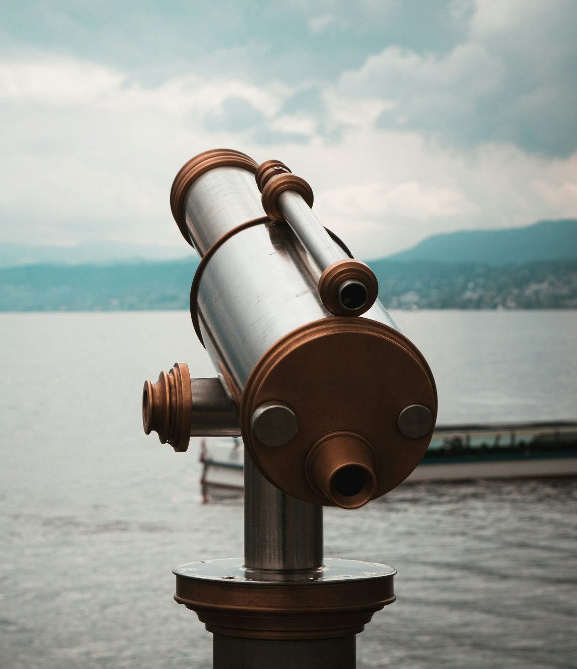 Symbolfoto Fernrohr Teleskop am Ufer mit Blick auf einen See und bewölkten Himmel.